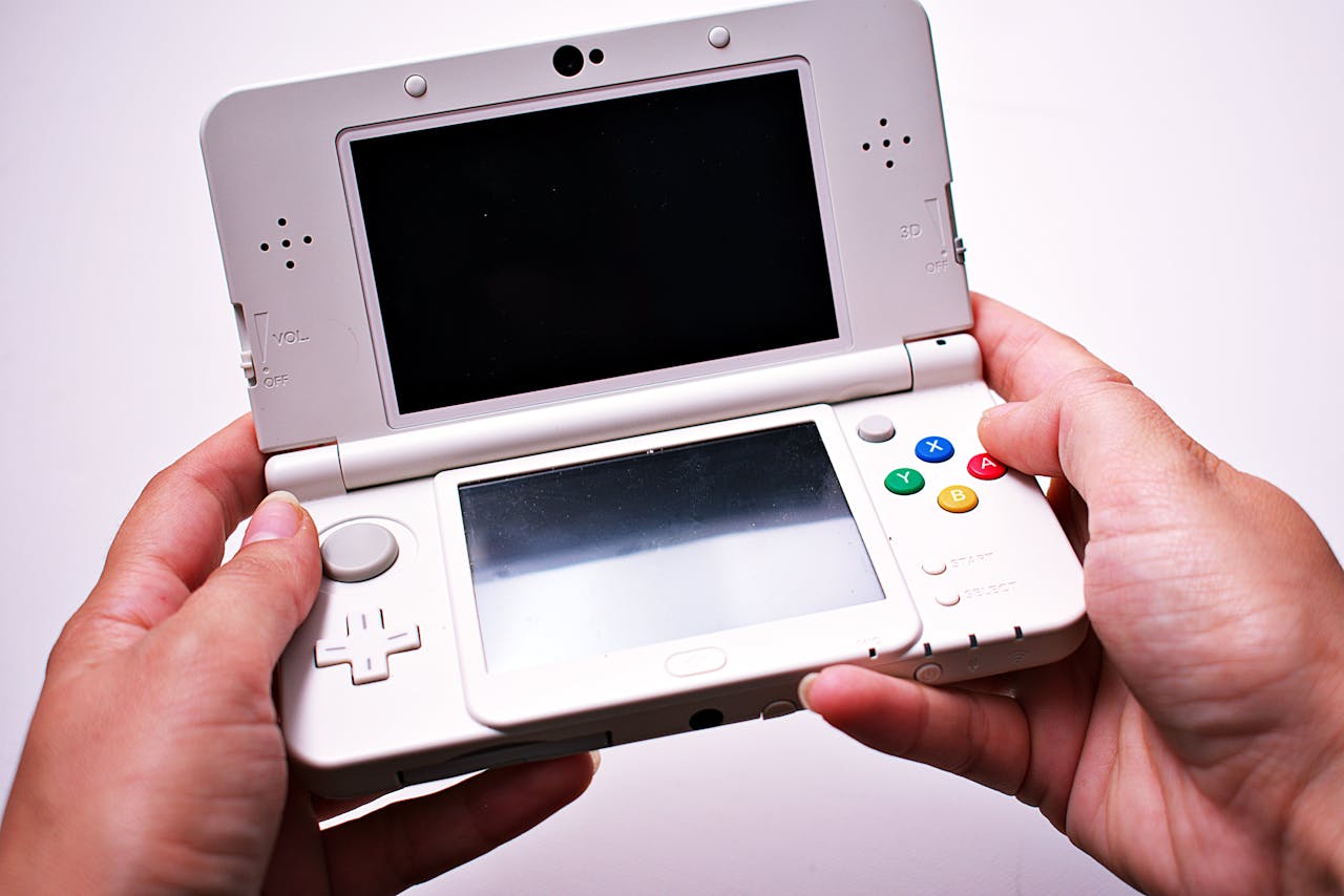 services-06 Close-up of hands holding a white portable gaming console with dual screens.